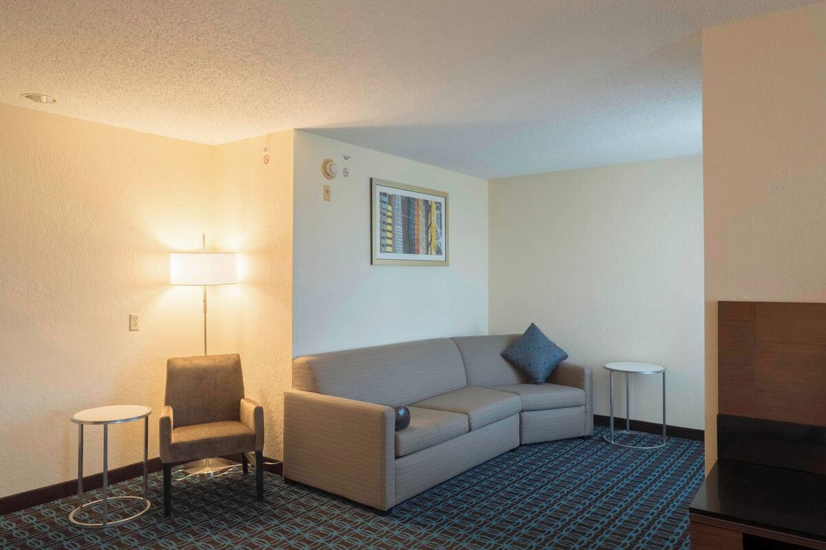 A hotel room with a sofa, armchair, small round table, and a TV stand.
