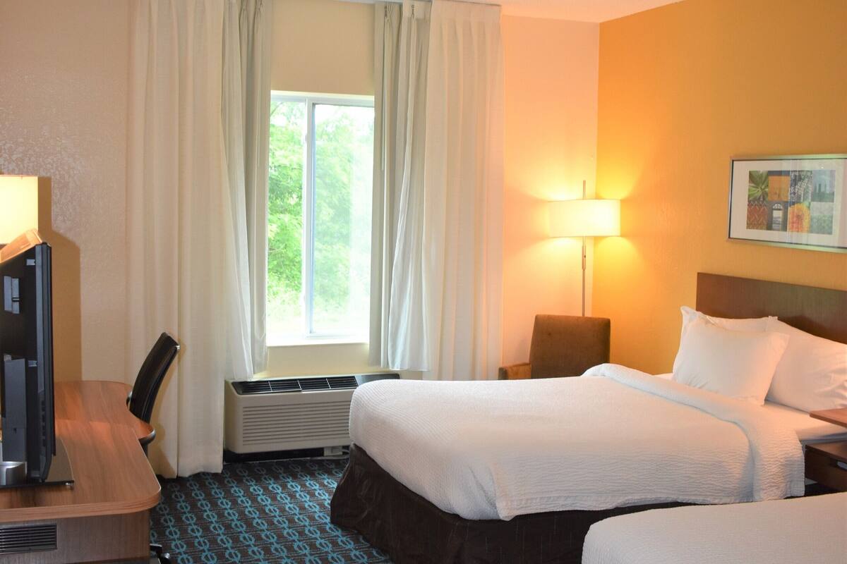 A hotel room with a bed, a desk, a chair, a lamp, and a window with curtains.