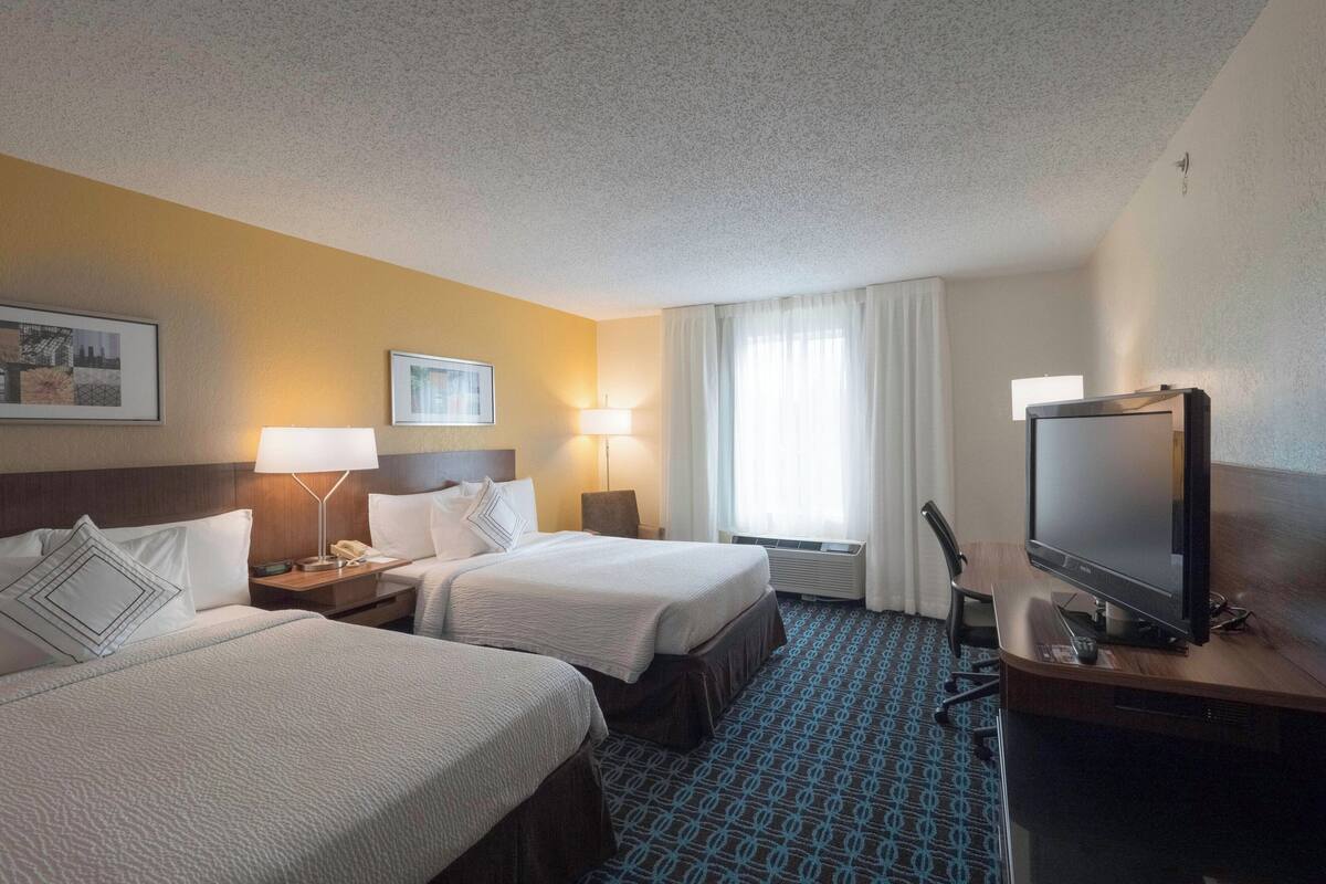 A hotel room with two beds, a desk with a television, and a window with curtains.