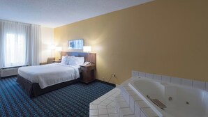 Ein Hotelzimmer mit einem großen Bett, einem Nachttisch mit Lampe, einem an der Wand montierten Fernseher und einem separaten Badezimmer mit Badewanne.