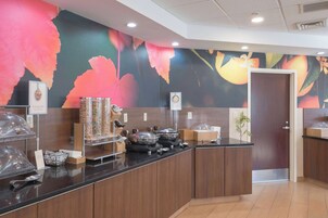 Zona de bufé con mostrador, recipientes para comida y una pared decorativa con motivos florales.