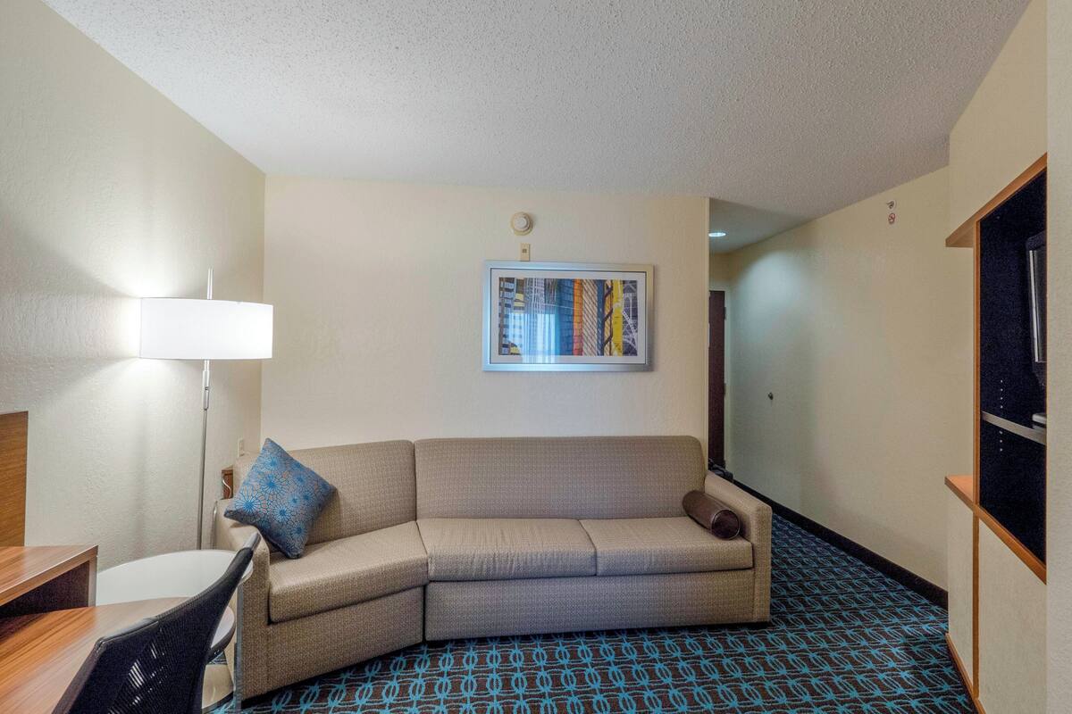 A hotel room with a sofa, a desk, a lamp, and a framed picture on the wall.