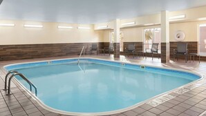 Una piscina con solárium empedrado, un cartel que prohíbe los saltos y una zona de estar con sillas y mesas.
