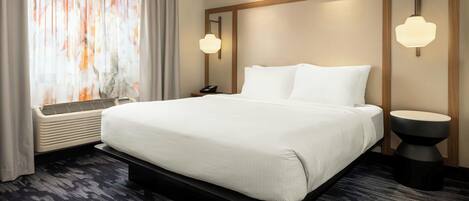 A hotel room with a large bed, a bedside table, a wall-mounted light, and a window with curtains.
