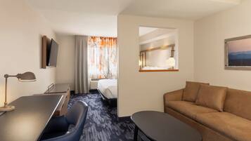 A hotel room with a bed, a desk with a chair, a sofa, a small table, and a TV mounted on the wall.