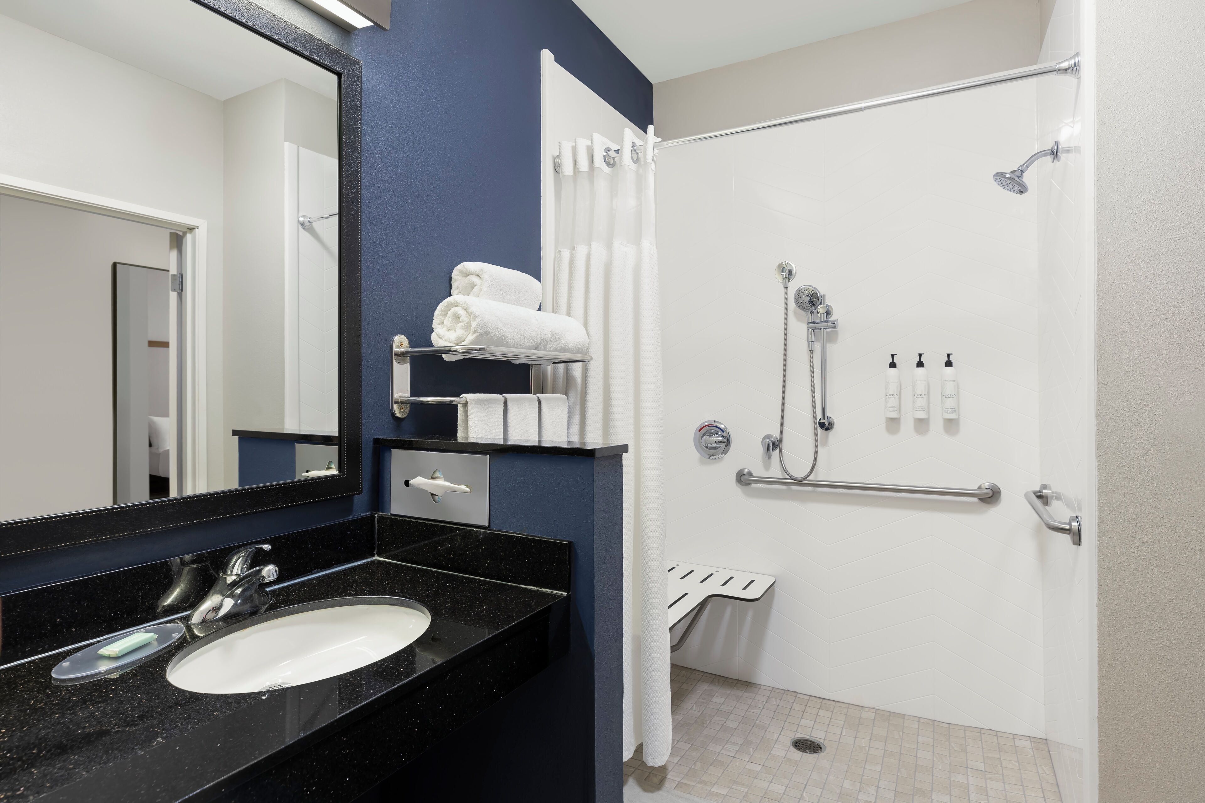 Un baño moderno con lavamanos de encimera negro, un espejo, ducha con cabezal de ducha manual y un perchero.