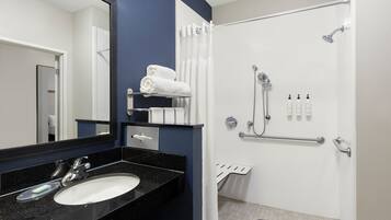 Un baño moderno con lavamanos de encimera negro, un espejo, ducha con cabezal de ducha manual y un perchero.