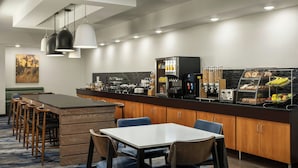 Una habitación de hotel moderna con comedor que incluye una barra, armarios de madera y un conjunto de asientos.