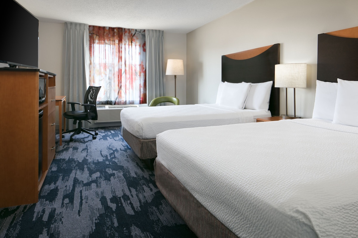 A hotel room with two beds, a desk with a chair, a TV, and a window with curtains.