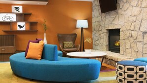 Un salón moderno con un sofá azul, un sillón de cuero marrón, una mesa de centro redonda y una pared de chimenea de piedra.