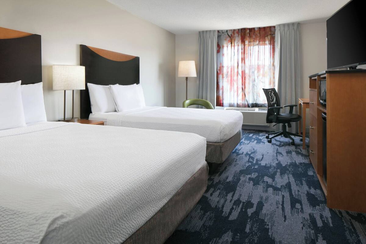 A hotel room with two beds, a desk, a chair, a television, and a window with curtains.