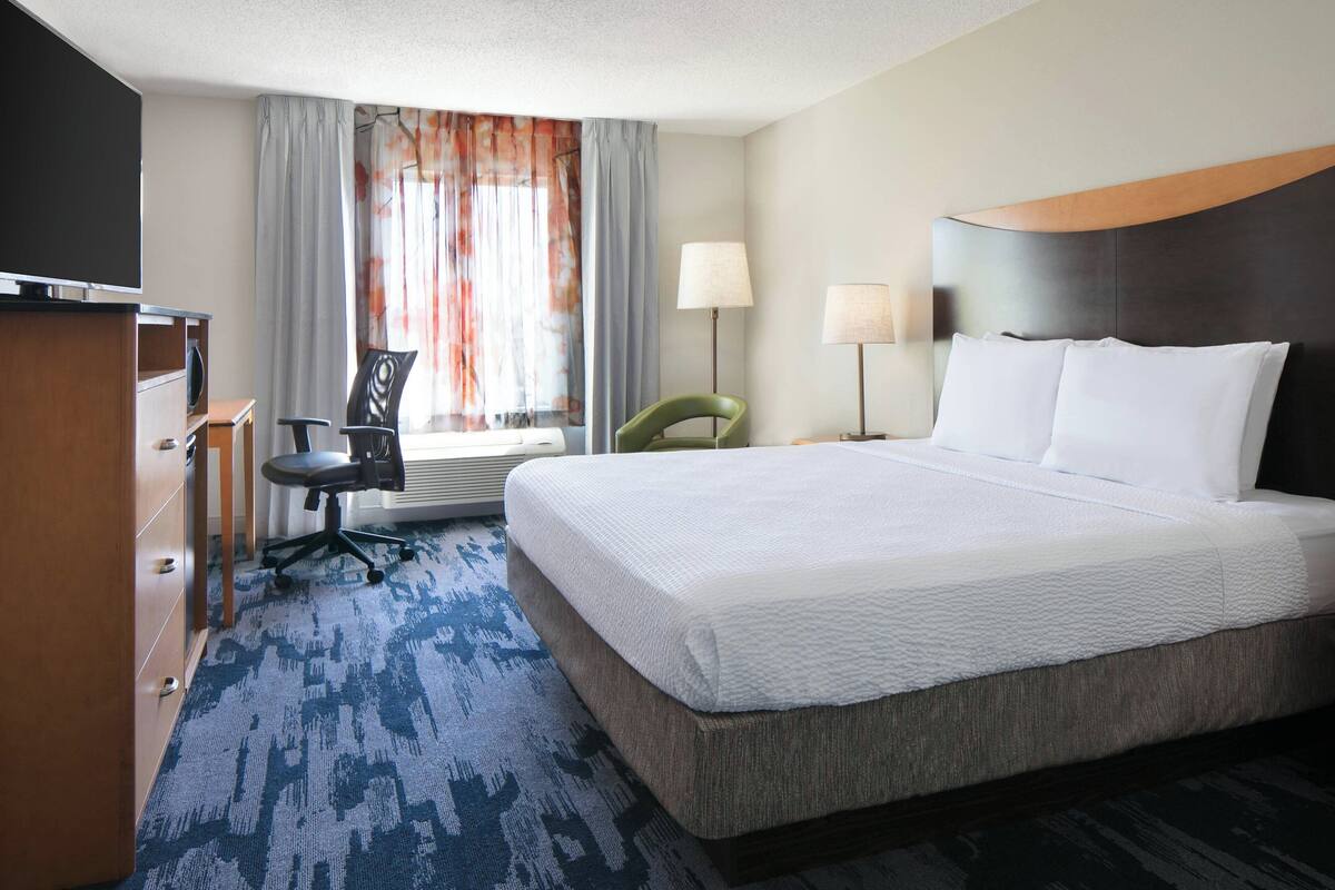 A hotel room with a large bed, a desk, a chair, a TV, and a window with curtains.