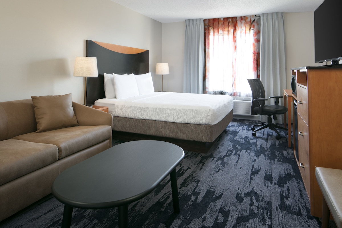 A hotel room with a bed, a sofa, a desk, and a television.