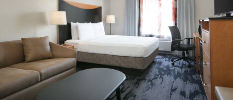 Ett hotellrum med en säng, en soffa, ett skrivbord och en tv.