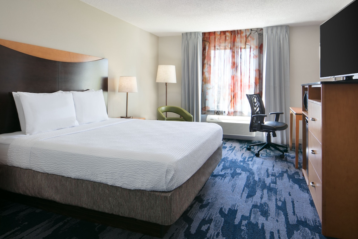 A hotel room with a large bed, a desk, a chair, a TV, and a window with curtains.