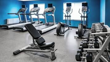 Un gimnasio con cintas de correr, elípticas, una prensa de banca y mancuernas.