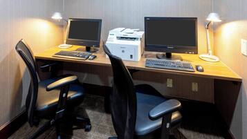 Een hotelkantoor met twee computermonitoren, een printer, een toetsenbord en twee bureaustoelen.