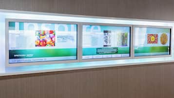 A digital display with three screens. Each screen features an article with a title, an image, and some text. The first screen has a colorful image with the title 'Pat Bailey'. The second screen shows an article titled 'Janet A. Hines'. The third screen displays an article with a title 'Chica Chips'.