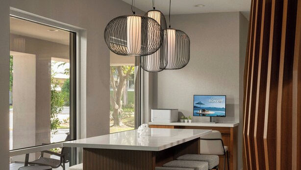 A modern kitchen with a large island, pendant lighting, and a flat-screen TV displaying 'Marriott Bonvoy'. - Springhill Suites By Marriott Houston Brookhollow (Houston)