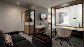 Une chambre d’hôtel moderne équipée d’un canapé, d’un bureau, d’un miroir, d’une télévision et offrant une vue sur l’extérieur.