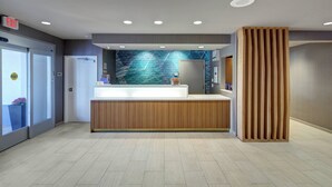 A reception area with a wooden counter, a wall with a digital display, and a large window. - SpringHill Suites Port St. Lucie (Port Saint Lucie)