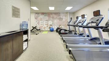 Un gimnasio con cintas de correr, pelotas de ejercicio y un dispensador de agua.