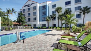A hotel with a swimming pool, green lounge chairs, and palm trees. - SpringHill Suites Port St. Lucie (Port Saint Lucie)