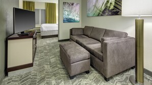 A hotel room with a sofa, ottoman, flat-screen TV, and artwork on the walls. - SpringHill Suites Port St. Lucie (Port Saint Lucie)