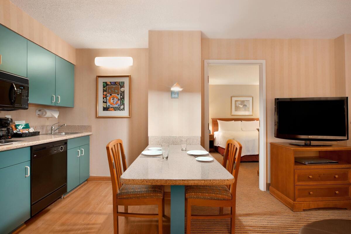 A compact hotel room with a kitchenette, dining area, and a TV.