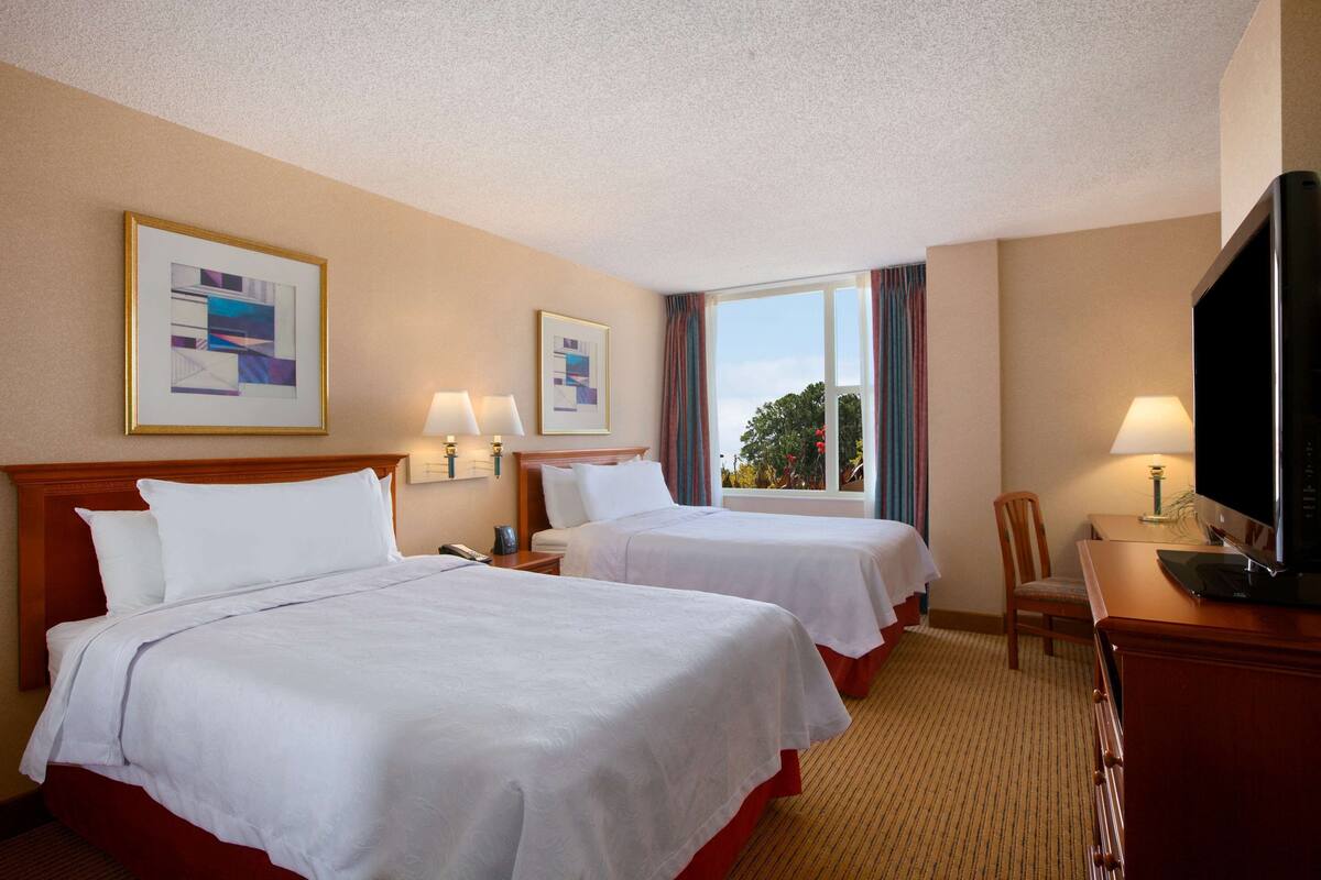 A hotel room with two beds, a television, a desk, and a window with curtains.