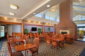A spacious indoor dining area with wooden tables and chairs, a brick fireplace, and a large window providing natural light. - Homewood Suites by Hilton Falls Church - I-495 at Rt. 50 (Falls Church)