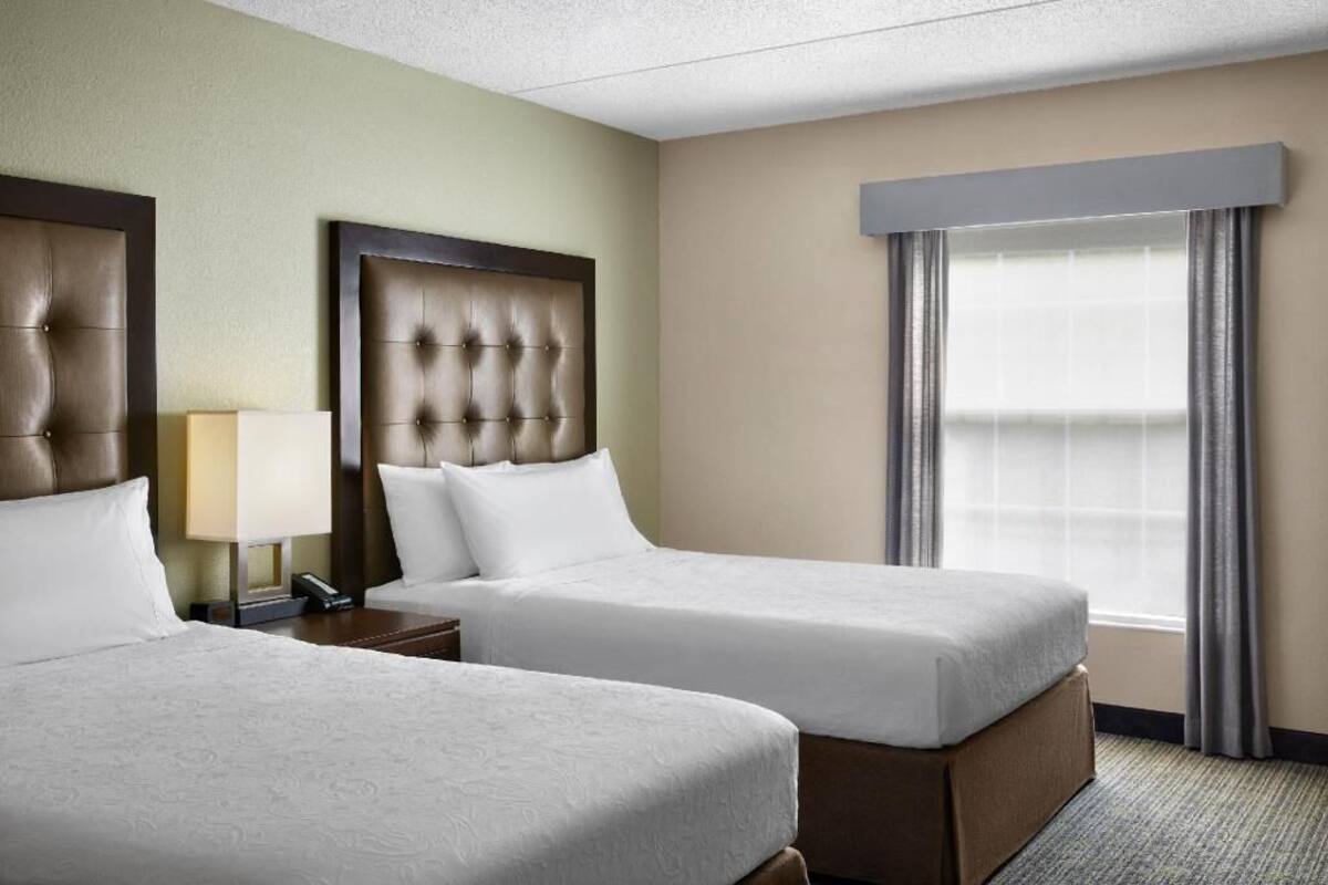 Une chambre d’hôtel avec deux lits, une table de chevet, une lampe et une fenêtre avec des rideaux.