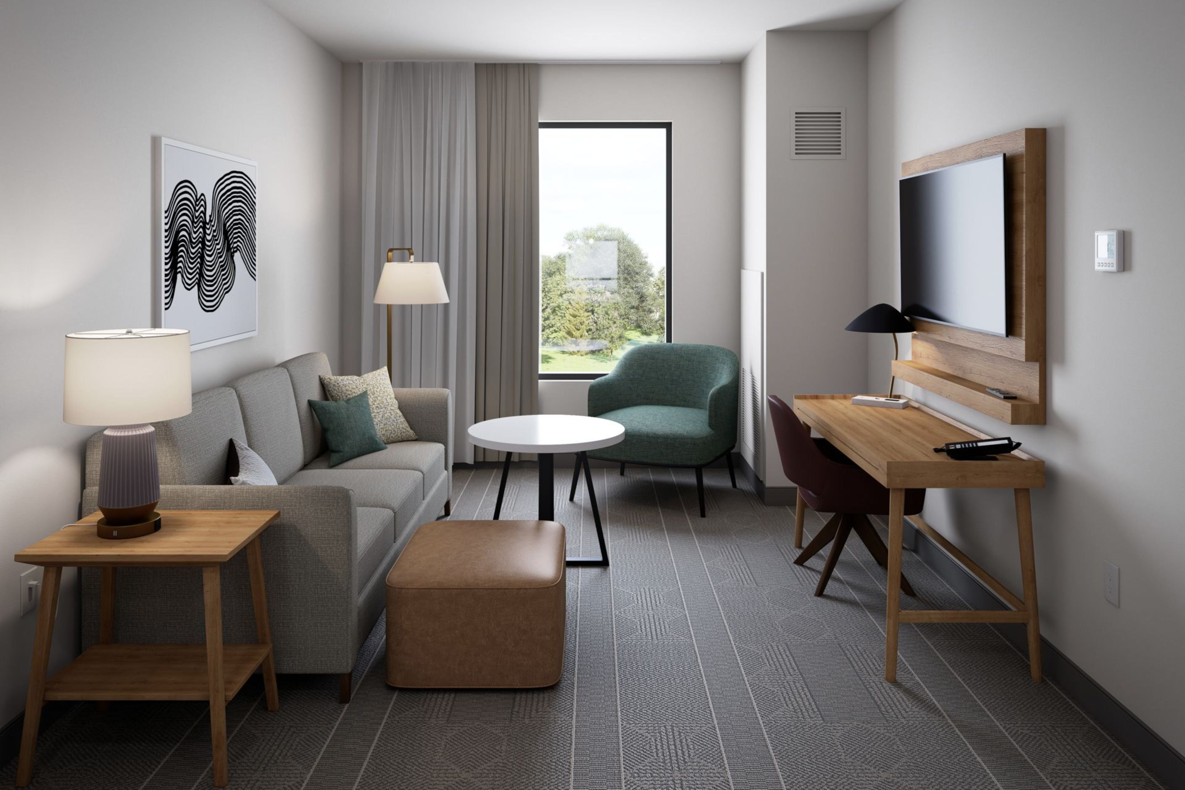 A modern hotel room with a sofa, a round table, a green armchair, a TV, and a window with curtains.