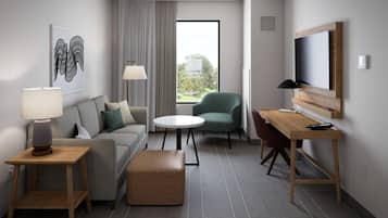 A modern hotel room with a sofa, a round table, a green armchair, a TV, and a window with curtains.