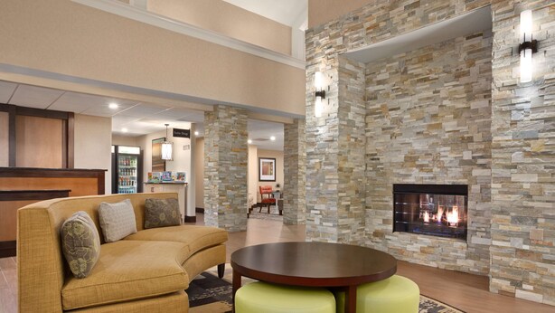 A lobby with a stone wall, a fireplace, a sofa, and a round table. - Homewood Suites Dallas/Park Central (Dallas)