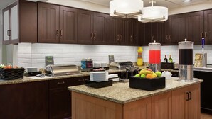 A modern kitchen with dark wooden cabinets, granite countertops, a built-in island with fruit, and a coffee station. - Homewood Suites Dallas/Park Central (Dallas)