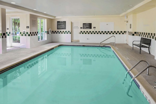 Una piscina interior rectangular con bordes de azulejos, un banco y señales de seguridad en las paredes.