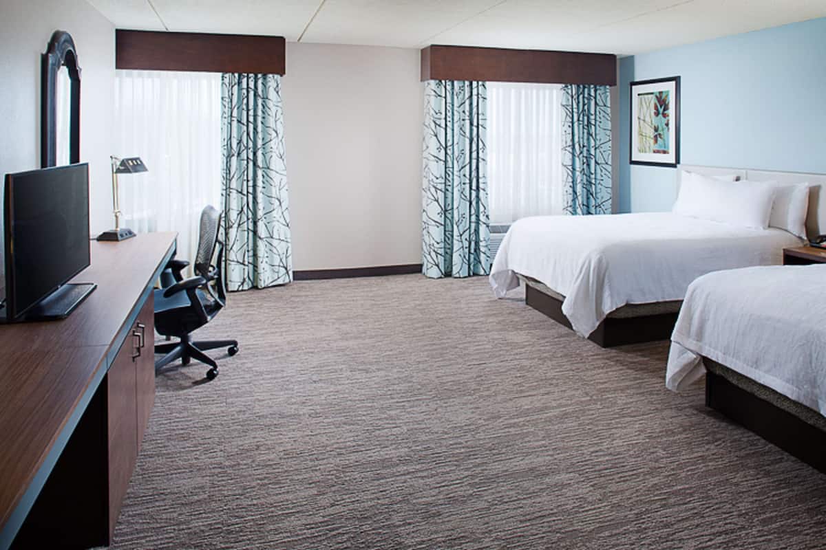 Una habitación de hotel con escritorio, dos camas, televisor y una silla.