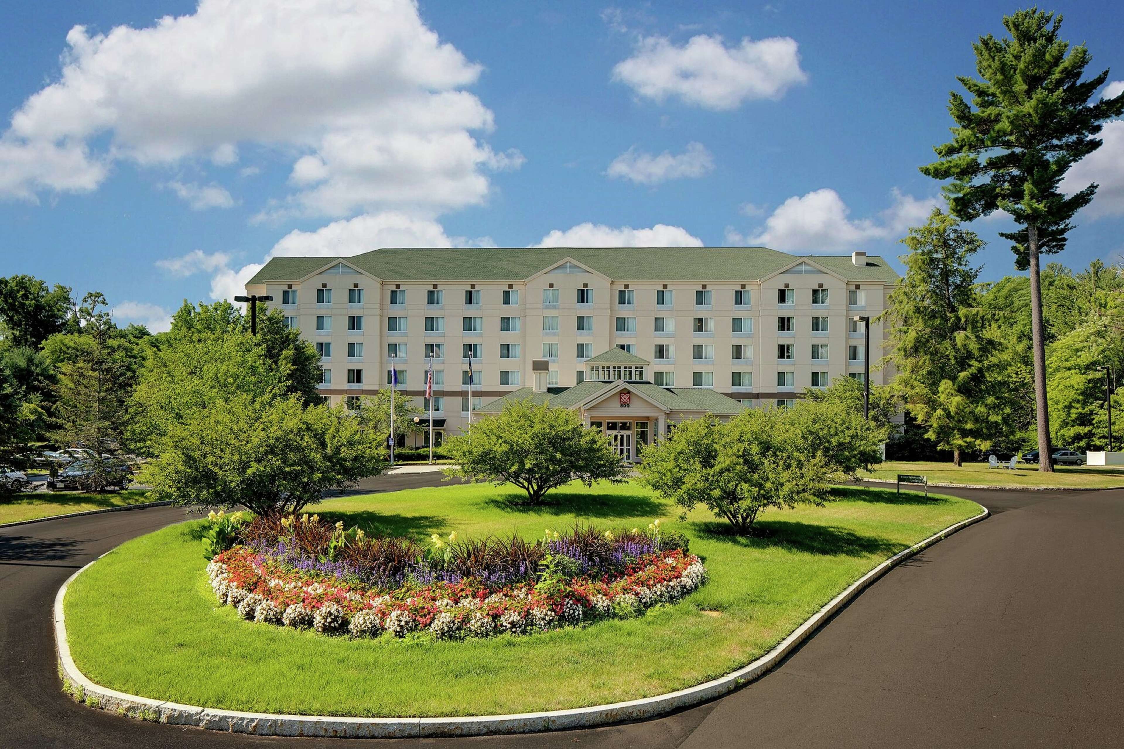 A multi-story hotel with a symmetrical facade, a central entrance with a portico, and a landscaped garden with a variety of flowers and shrubs.