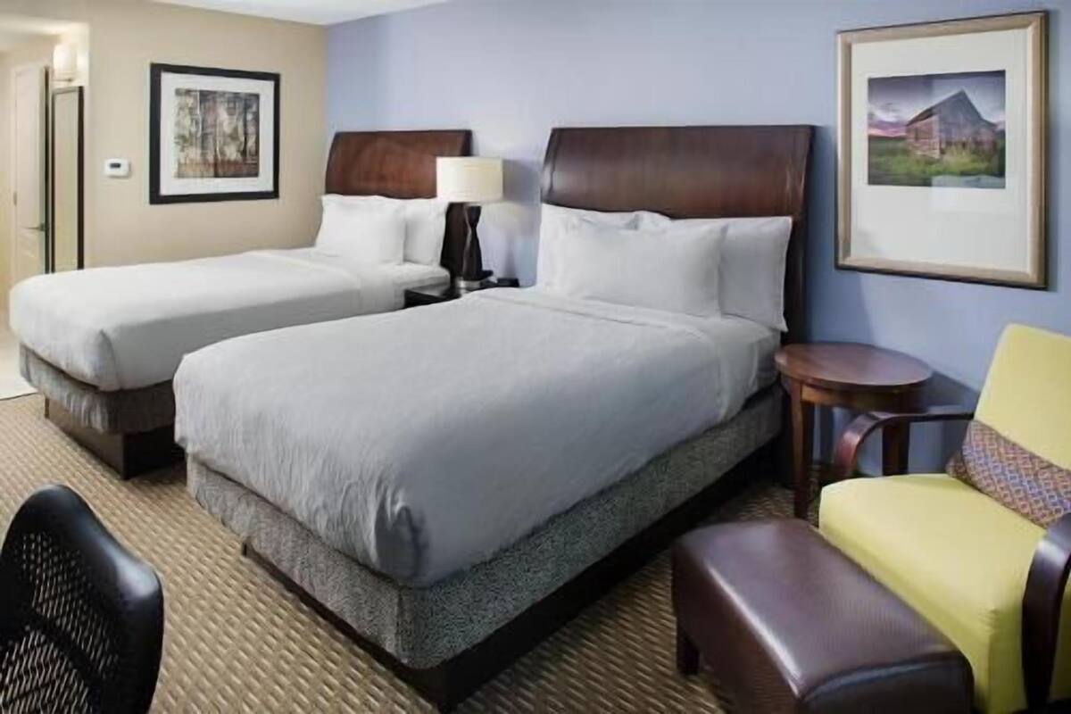 Une chambre d’hôtel avec deux lits, une petite table, une chaise et une lampe.