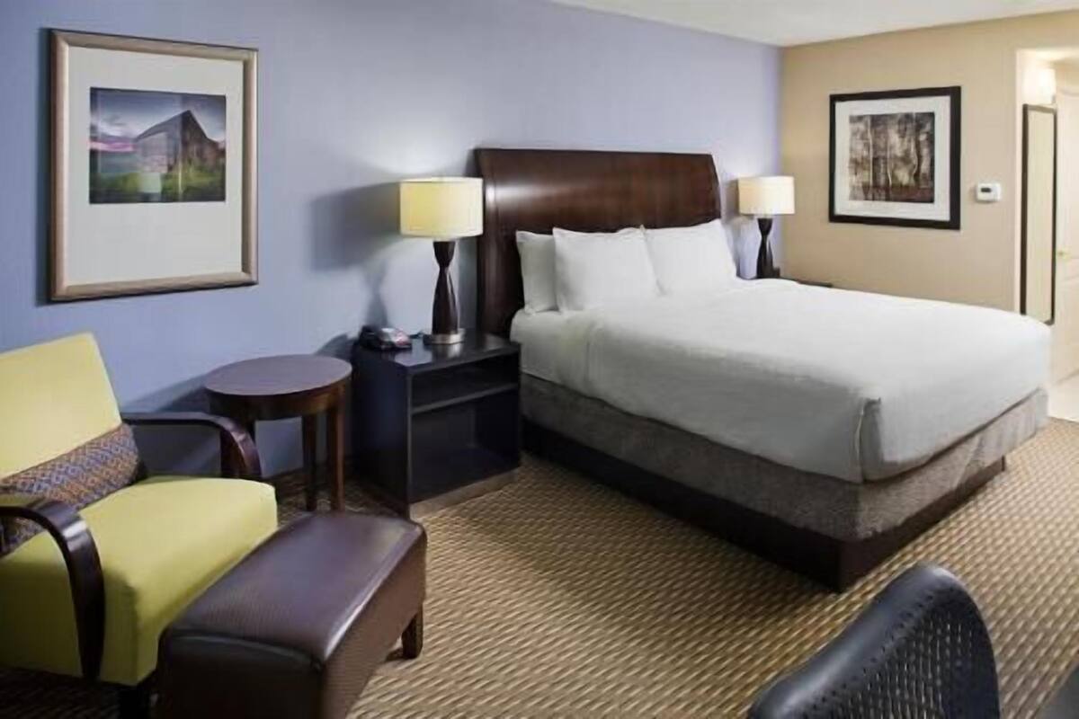 Une chambre d’hôtel comprenant un lit, deux tables de chevet avec des lampes, une chaise et une petite table.