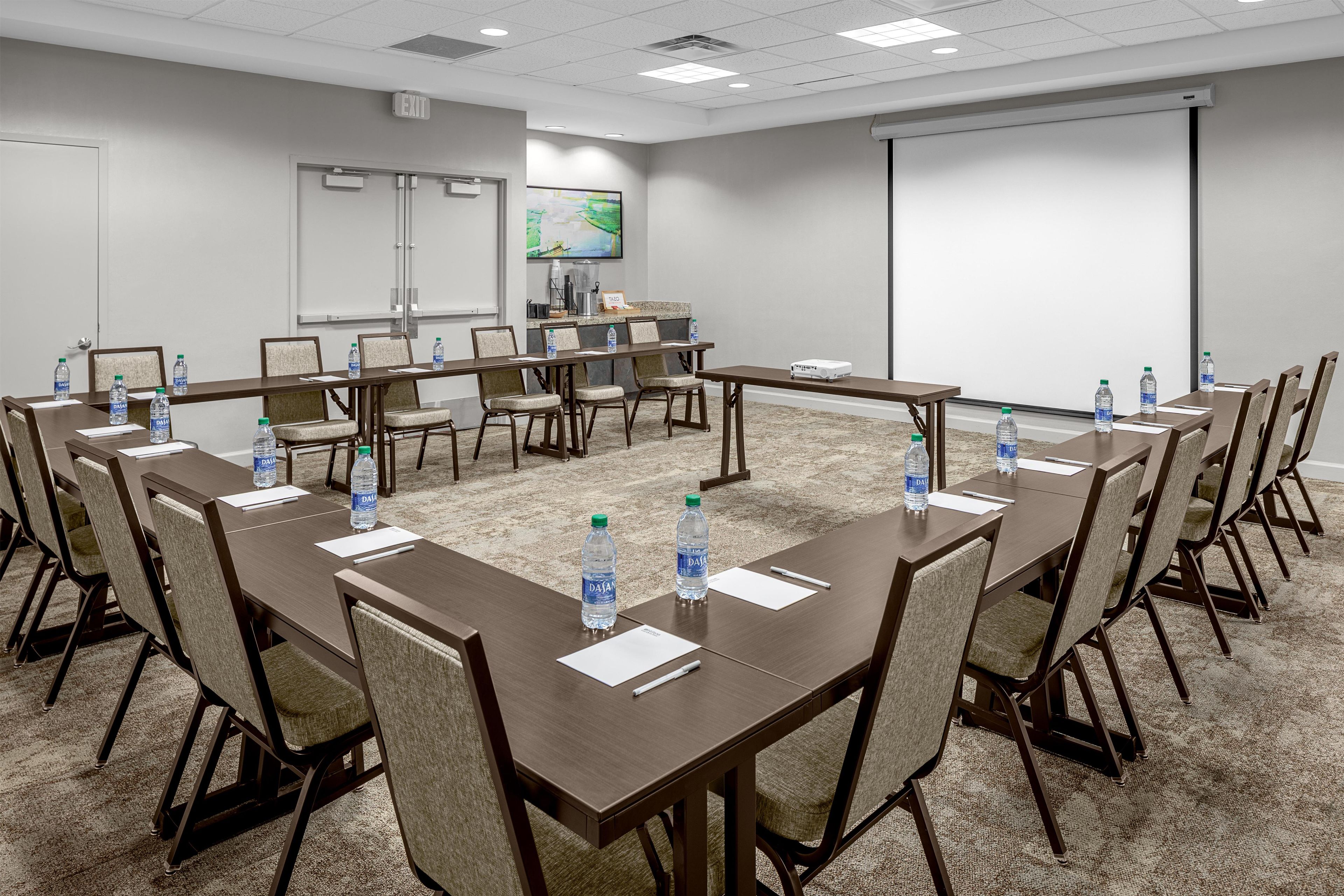 A conference room with multiple tables, chairs, water bottles, a projector, and a screen.