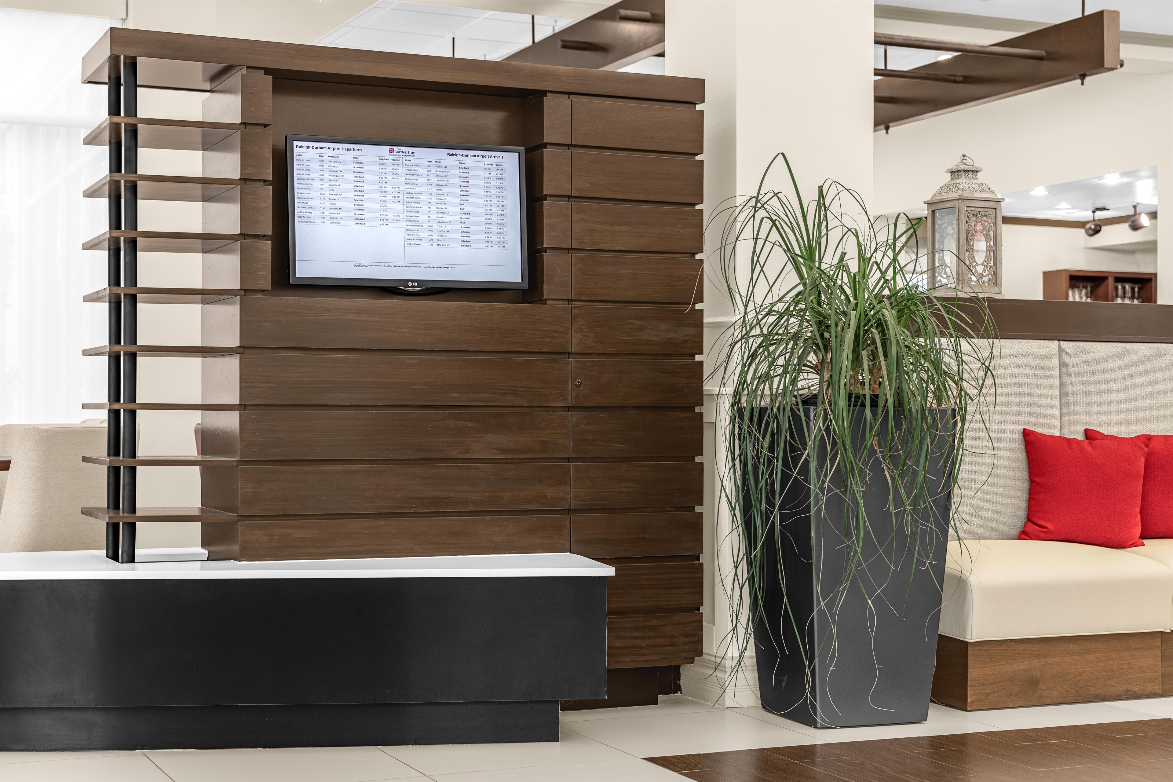 A reception desk with a digital display, a potted plant, and a sofa with red cushions.