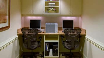 A home office with two desks, each with a computer and a chair, a printer, and a bookshelf with books and a vase.