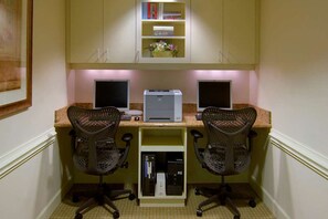 Ufficio domestico con due scrivanie, ciascuna dotata di un computer e una sedia, una stampante e una libreria con libri e un vaso.