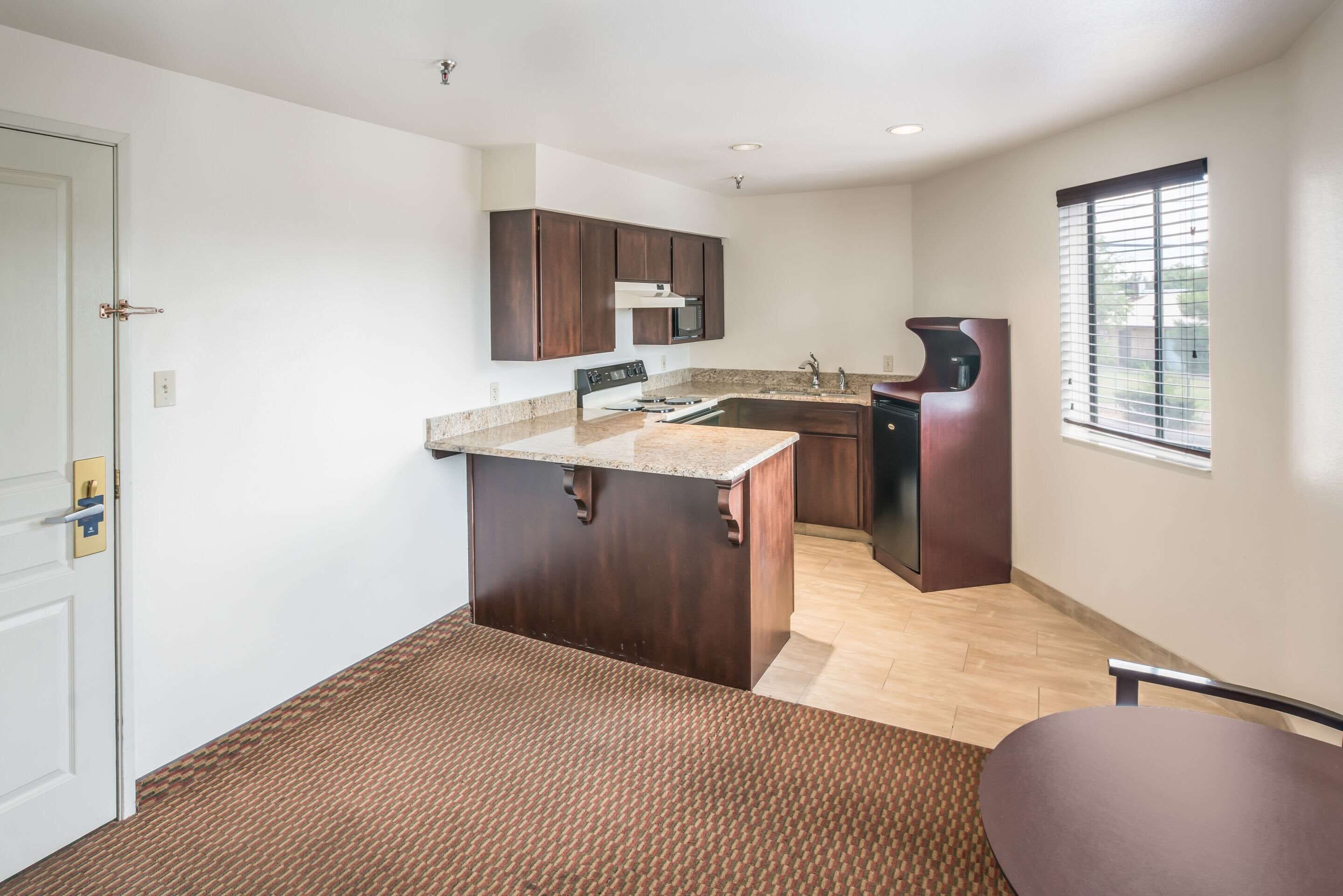 A compact kitchen with dark wood cabinets, a granite countertop, and a built-in microwave.