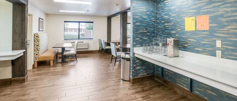 A modern kitchen with wooden flooring, a white countertop, and a blue textured wall.