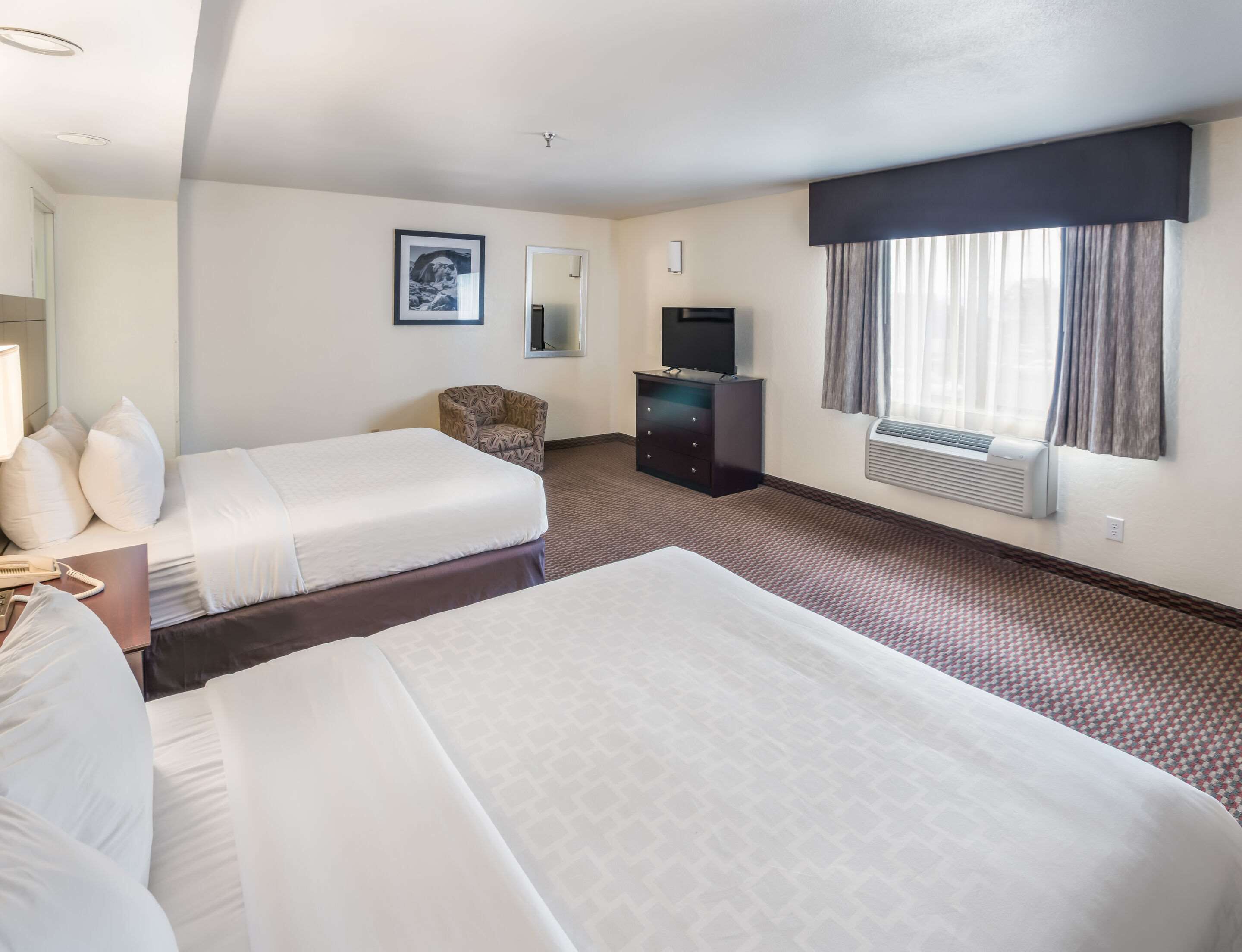 A hotel room with two beds, a desk, a chair, a TV, and a window with curtains.