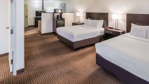 A hotel room with two beds, a desk, a chair, a lamp, and a small refrigerator.
