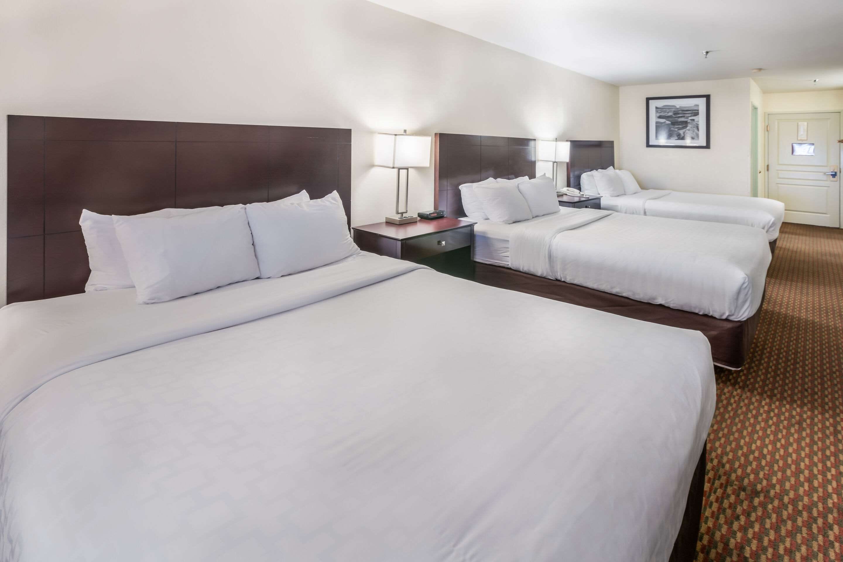 A hotel room with three single beds, each with a bedside table and lamp.